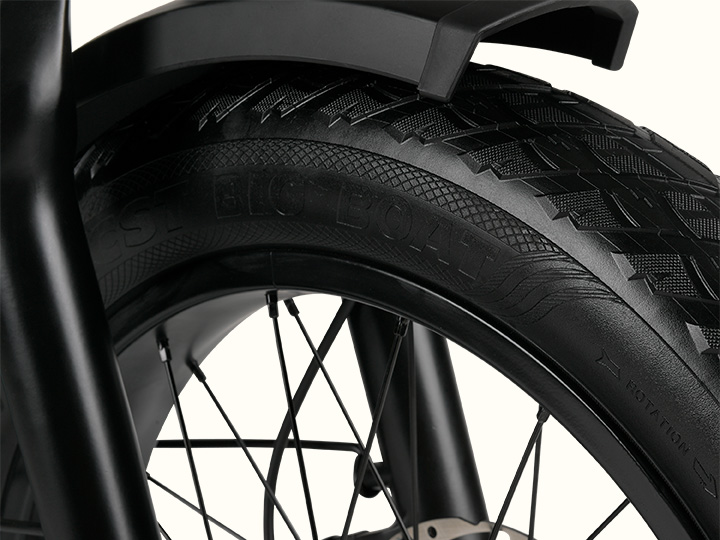 Close-up of an ebike's wheel, showcasing a thick, textured tire and sleek black fork, emphasizing durability and design.