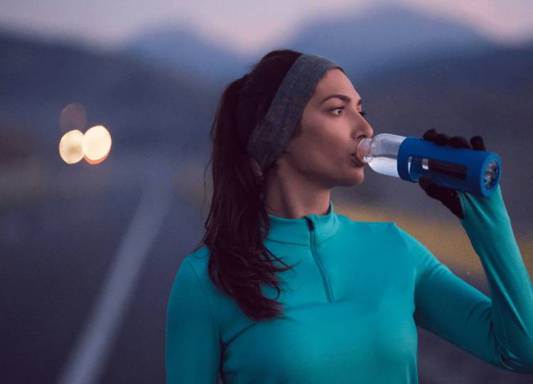 Recover from exercise with U Perform - lady drinking water from a bottle at dusk