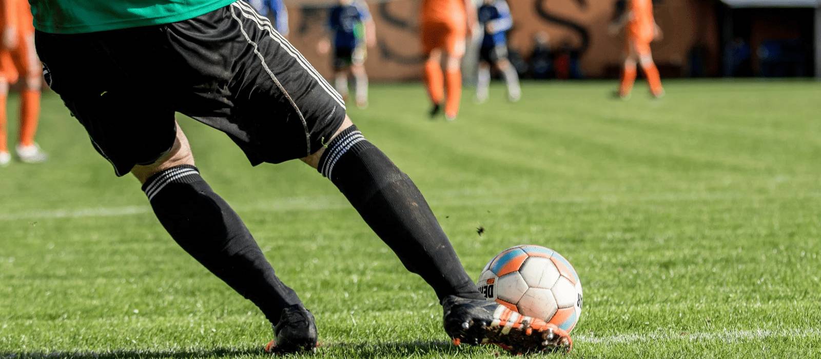 Male goalkeeper kicking football towards other male players - U Perform Football