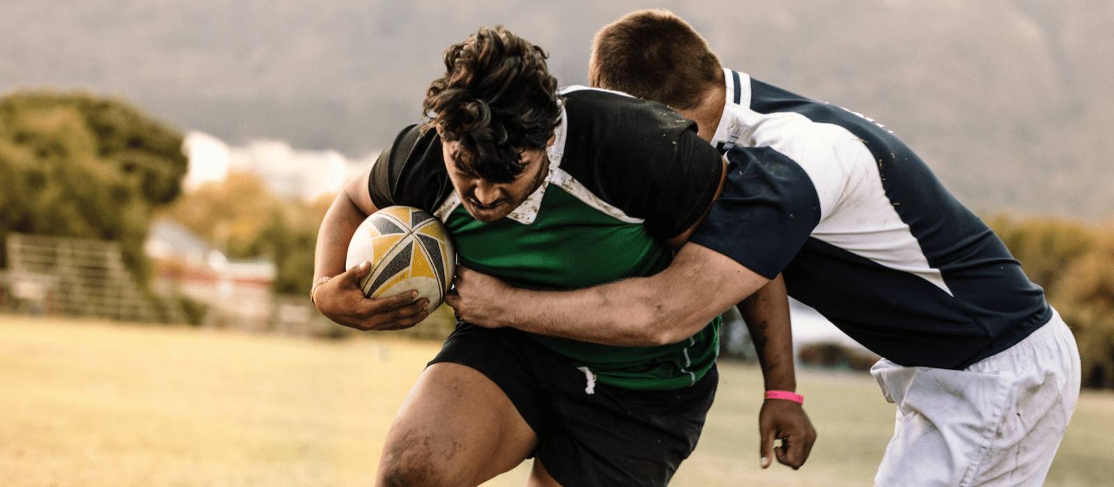 Two men playing rugby tackling while holding rugby ball