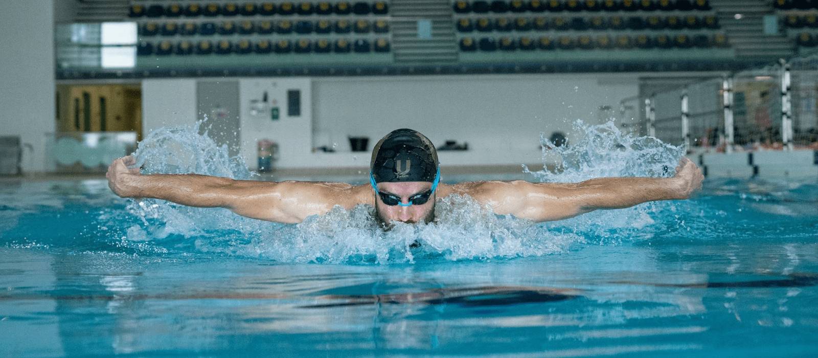 man swimming butterfly stroke in swimming pool wearing black and gold U Perform swimming cap