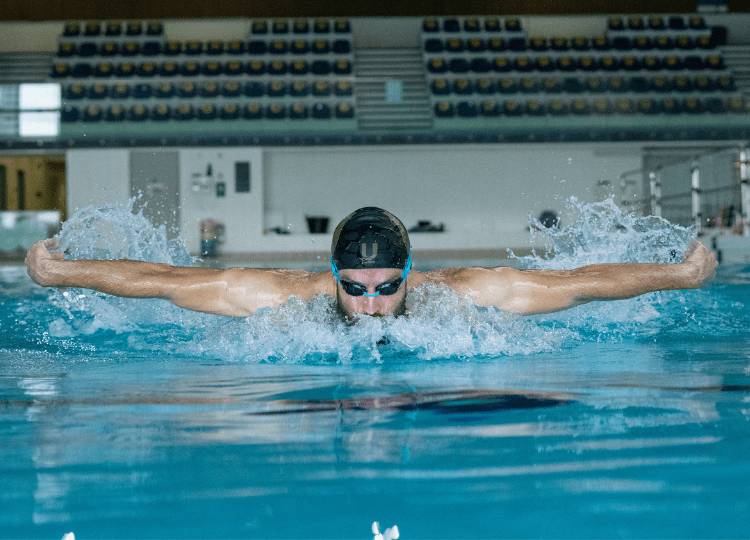 man swimming butterfly stroke in swimming pool wearing black and gold U Perform swimming cap