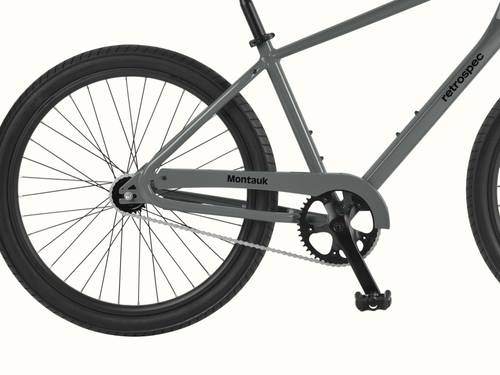Close-up of the rear wheel, chain, and pedal area of a gray retrospec Montauk bicycle against a white background.