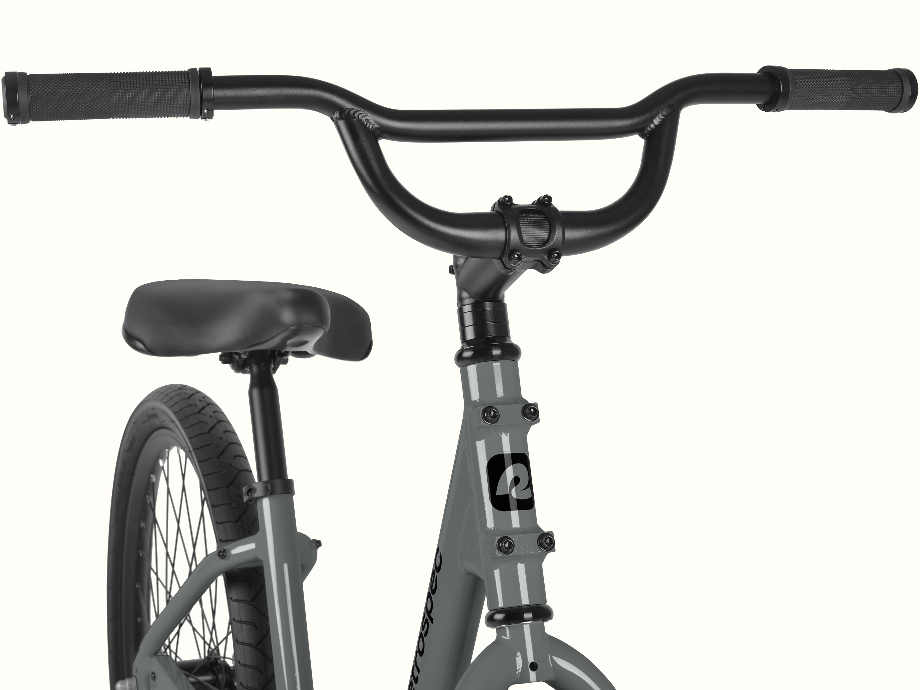Close-up of the retrospec Montauk step through's wide, BMX-style black handlebars with textured grips, paired with a sturdy stem and the retrospec head tube badge in Graphite.