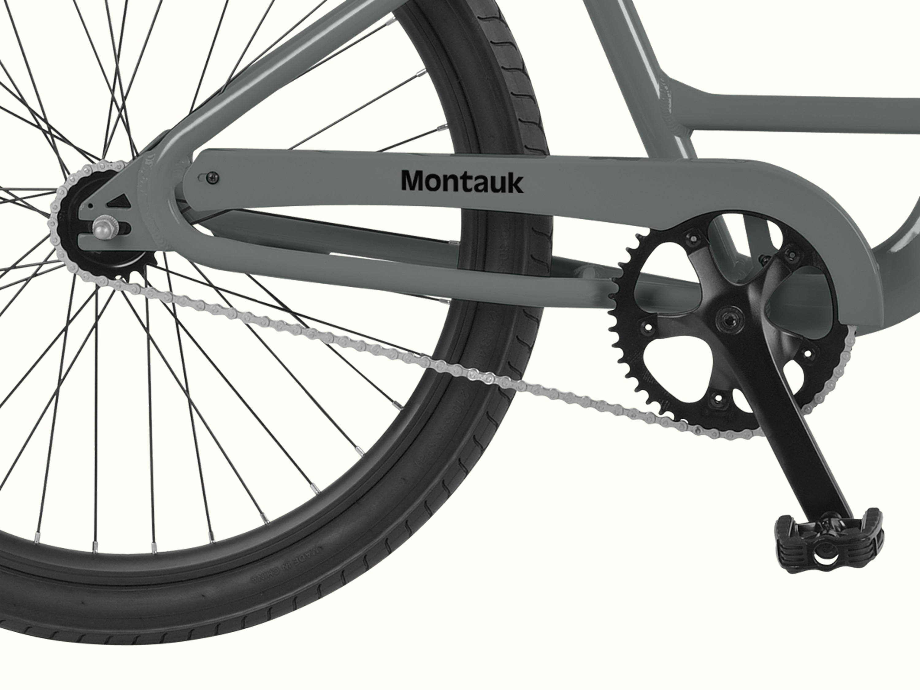 Close-up of the Montauk step through's single-speed drivetrain, featuring a black crankset, silver chain, and the iconic Montauk chainstay badge in Graphite.