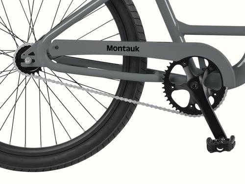 Close-up of the Montauk step through's single-speed drivetrain, featuring a black crankset, silver chain, and the iconic Montauk chainstay badge in Graphite.