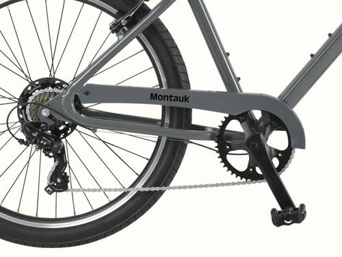 Close-up of the Montauk 26's Shimano 7-speed drivetrain, black alloy crankset, and rear cassette, with the Montauk name badge on the low-step graphite frame.