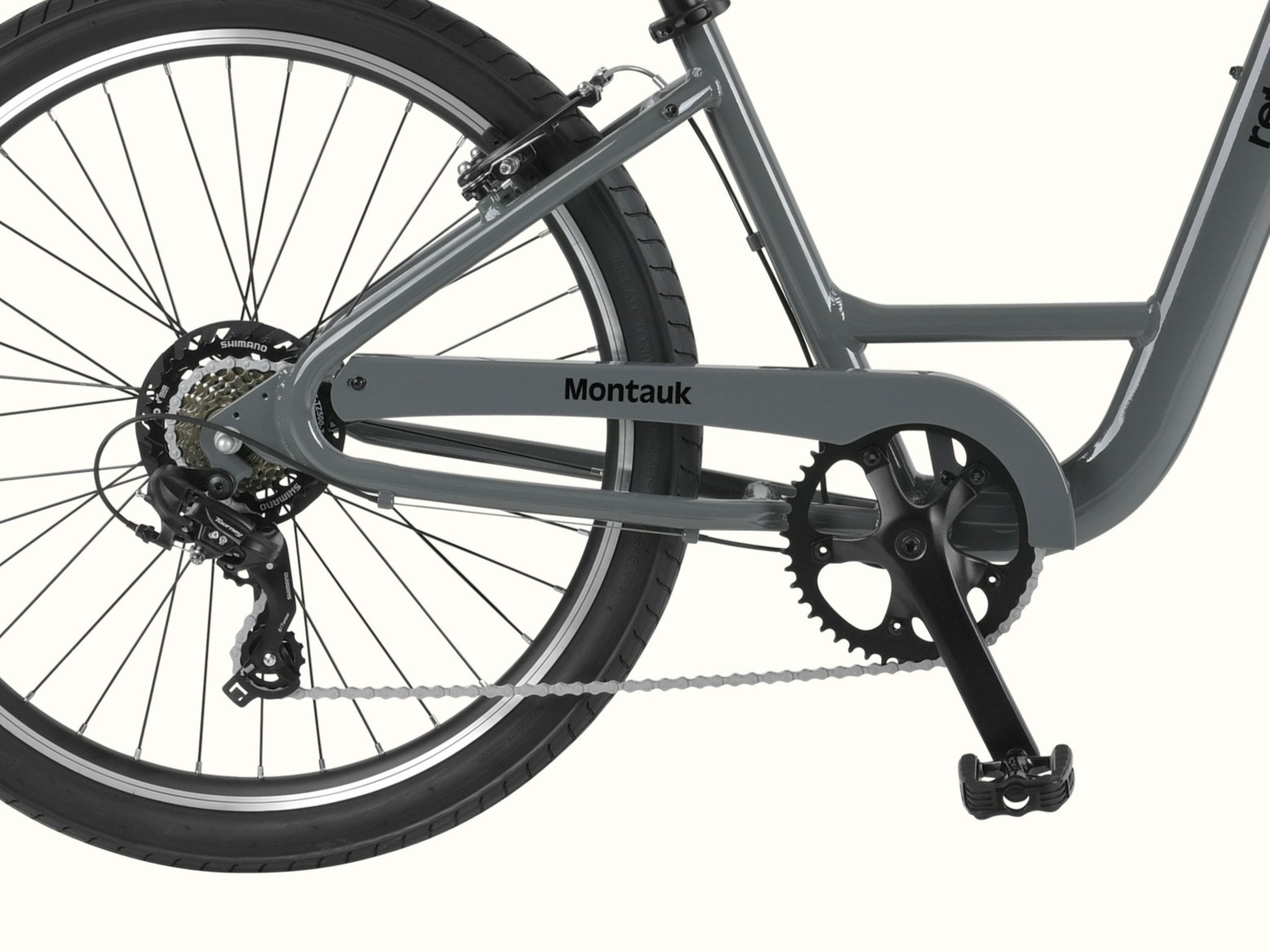 Close-up of the Montauk 26's Shimano 7-speed drivetrain, black alloy crankset, and rear cassette, with the Montauk name badge on the low-step graphite frame.