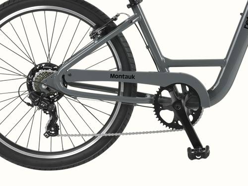 Close-up of the Montauk 26's Shimano 7-speed drivetrain, black alloy crankset, and rear cassette, with the Montauk name badge on the low-step graphite frame.