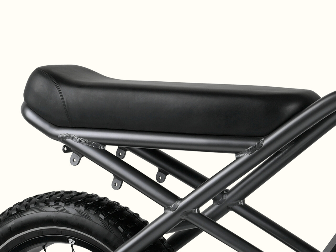 Close-up of a sleek black motorcycle seat mounted on a metal frame, showcasing a rugged tire in the background.
