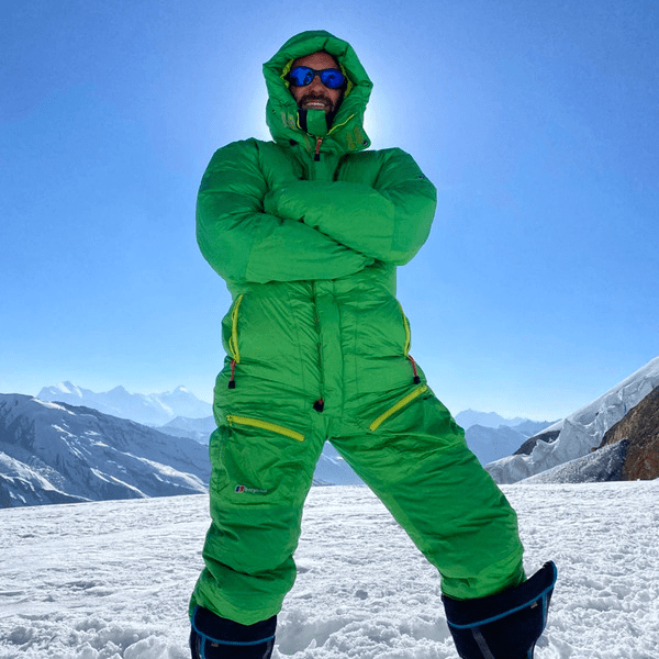 Arron Collins-Thomas standing at the top of a snowy mountain in green mountain gear and sunglasses
