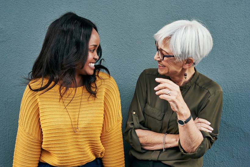 Two women talking.  One younger woman talking to a mature older lady.  They are both relaxed and laughing as they chat