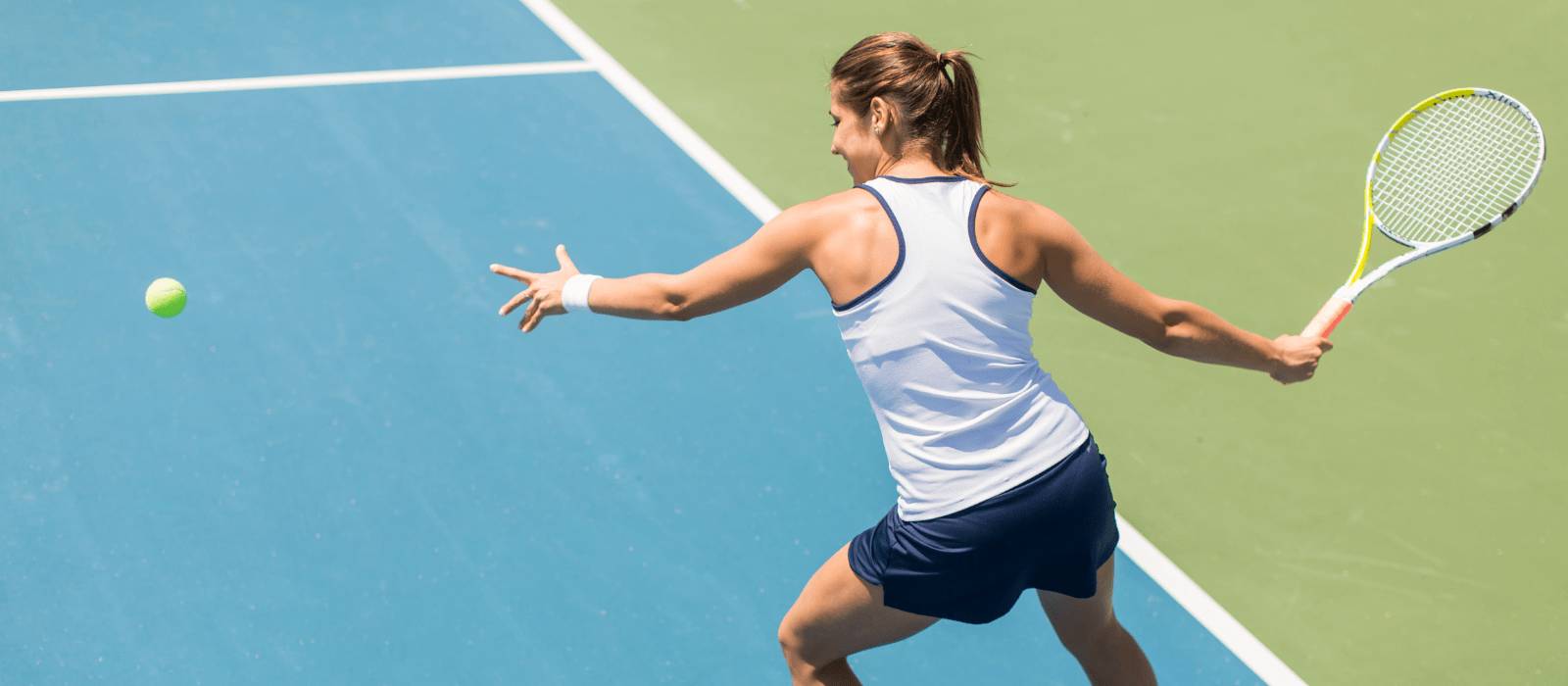 U Perform Tennis - female tennis player mid swing as a tennis ball comes towards her over a blue tennis court