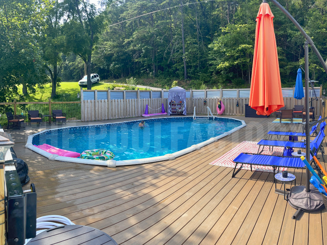 Backyard oval saltwater swimming pool with an umbrella and sun loungers on a full wrap around deck