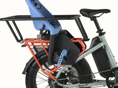 Close-up of the retrospec Roo Rev electric cargo bike showing a blue child seat, wheel guard set, and orange rear rack with integrated battery.
