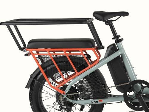 Close-up of the retrospec Roo Rev electric cargo bike showing the black passenger seat pad installed on the orange rear rack with wheel guard set and passenger handrail for safety.
