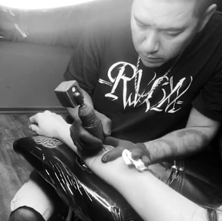 Tattoo artist using machine on person's forearm.