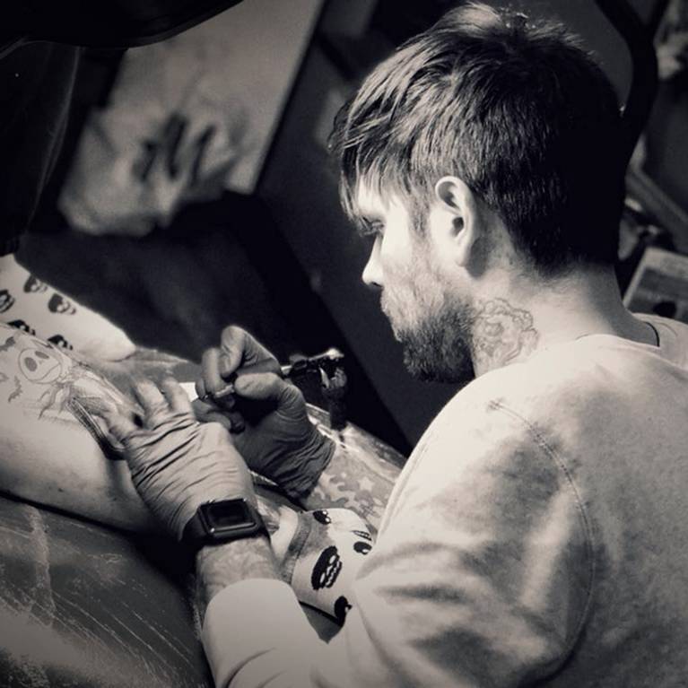 Tattoo artist working on a client's arm in a studio.