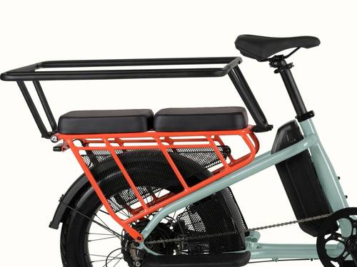 Close-up of the retrospec Roo Rev XL electric cargo bike showing the black passenger seat pad installed on the orange rear rack with wheel guard set and passenger handrail for safety.