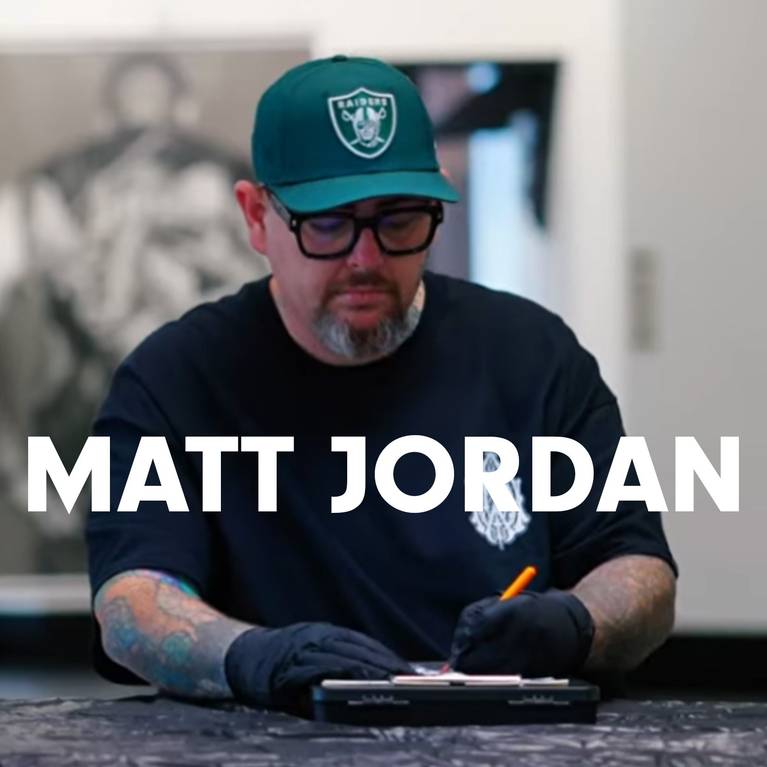 Man in cap and glasses writing, wearing gloves and a dark T-shirt.