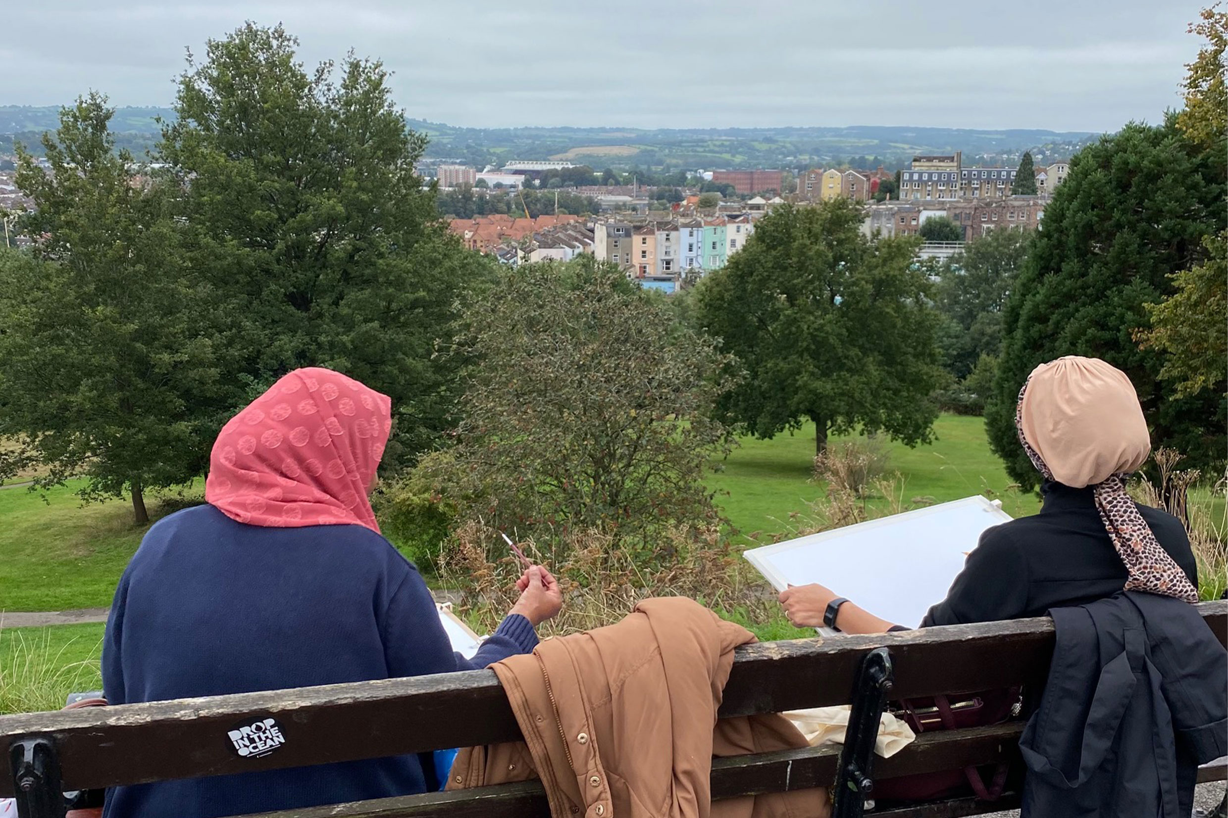 An image of two women on a bench drawing the Bristol skyline 