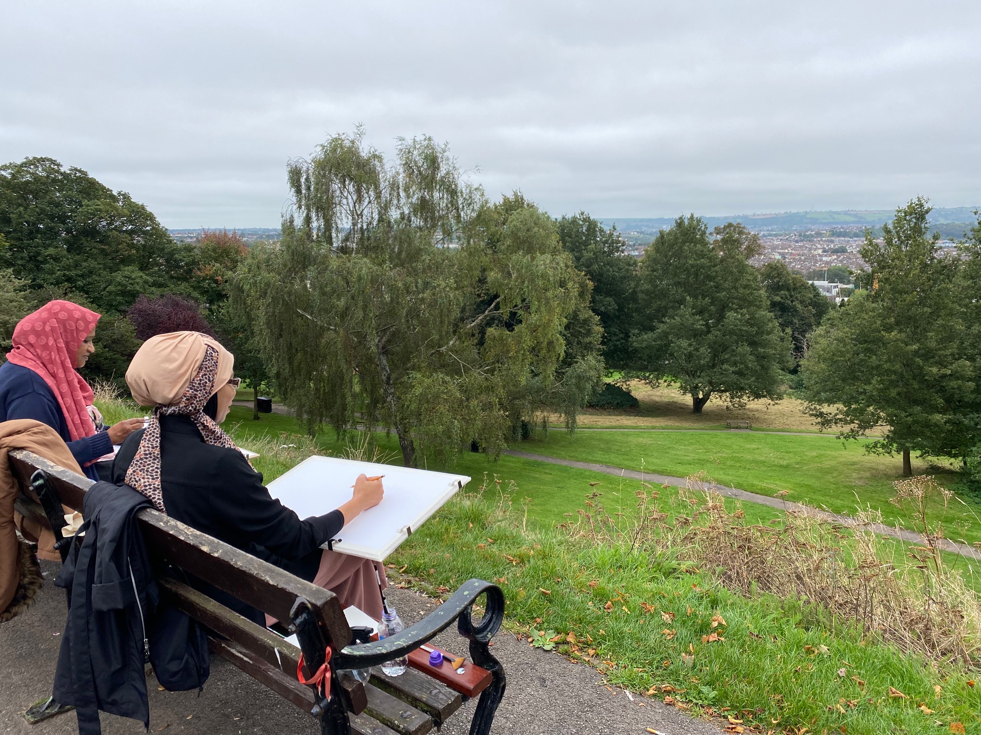 An image of two women on a bench drawing the Bristol skyline 