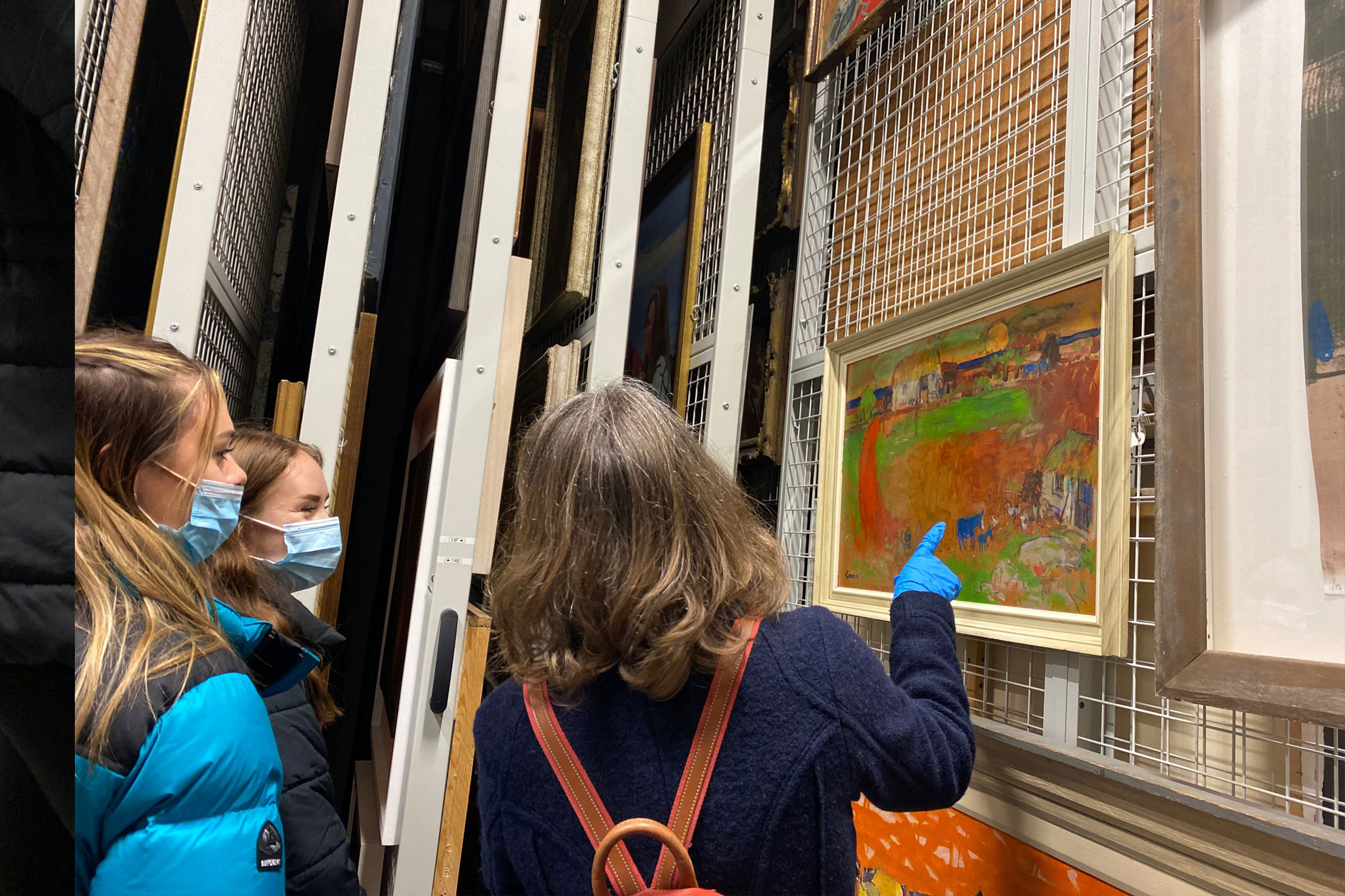 An image of three women looking at a painting in an art store room 