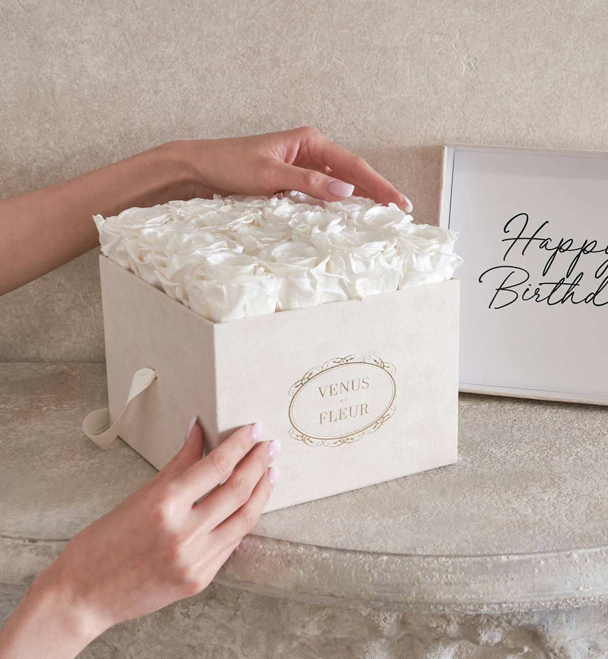 Hands reaching out, touching a white Venus et Fleur birthday gift box filled with white roses