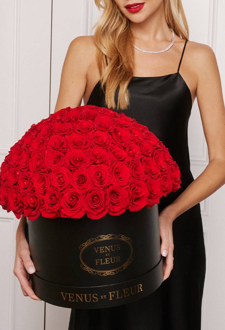 woman in black dress holding a black gift box with many red roses