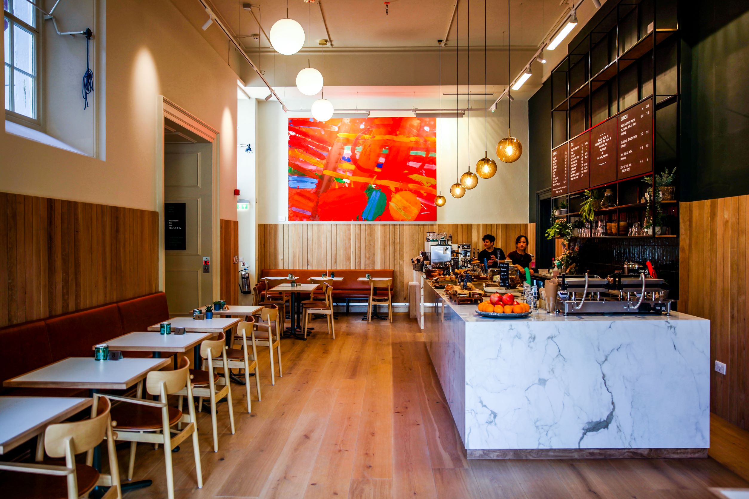 Internal view of the RWA cafe space featuring a marble counter, chairs & tables and a large red abstract painting on the far wall 