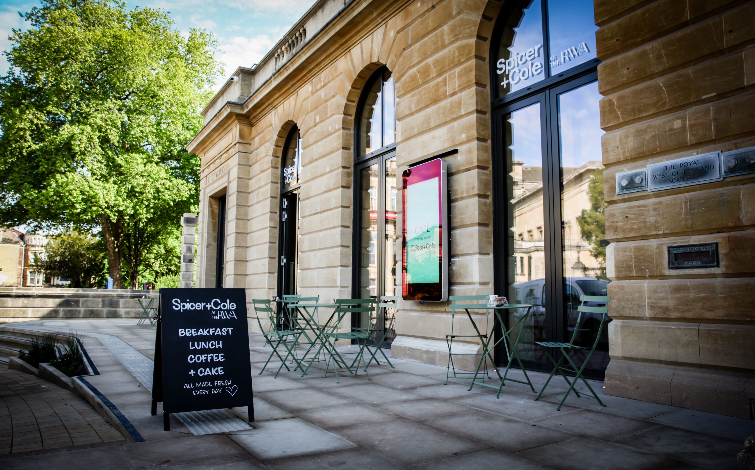 Outside the RWA cafe space on the forecourt with tables & chairs & a blackboard with with Spicer+Cole at the RWA 