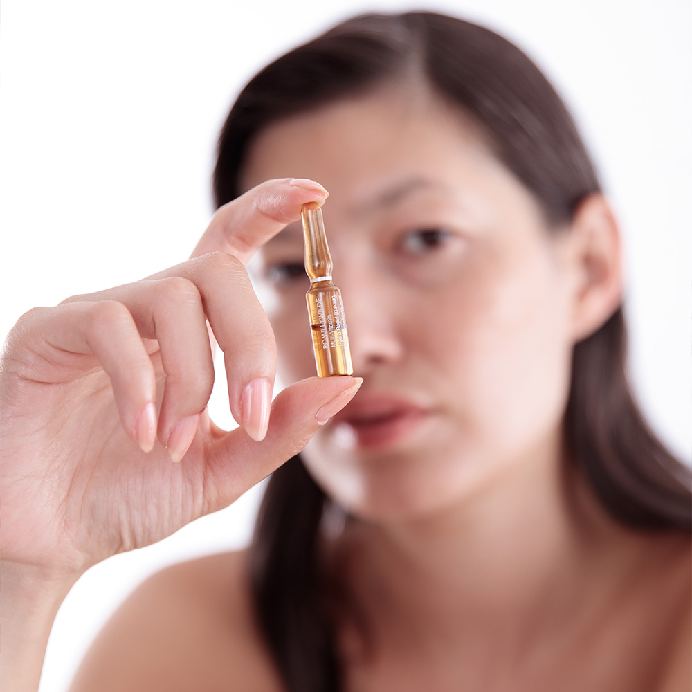 Woman Holding A Skincare Ampoule In Her Hand In Front Of Her Face