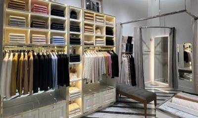 N.Peal Rockefeller store interior with illuminated shelves of neatly folded knitwear, racks of hanging garments, a central bench, and large mirrors reflecting the space
