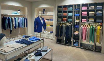 N.Peal Munich store interior with racks of colourful knitwear and jackets, shelves of neatly folded garments, a mannequin in a blue blazer, and display tables with folded clothing